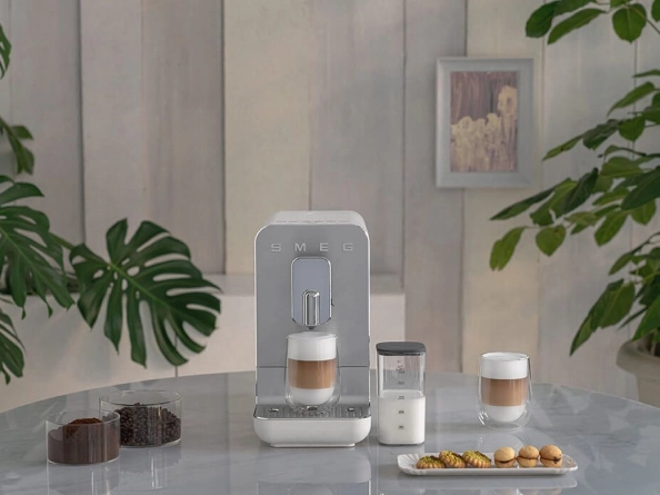 Smeg BCC12BLMEU вид спереди с готовым напитком и молочными аксессуарами на столе