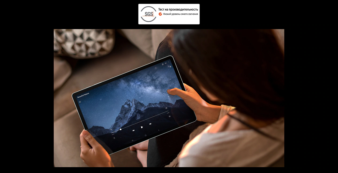 Женщина на диване держит обеими руками Galaxy Tab S9 FE+ и смотрит полноэкранное видео в горизонтальном режиме. Логотип SGS с надписью «Показатели проверены. Низкое излучение синего света».